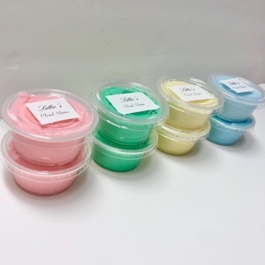 May include: A collection of eight small, round, clear plastic containers filled with colorful slime in shades of pink, green, yellow, and blue. Each lid features a white square label with the black printed text Lillie's Cloud Slime.