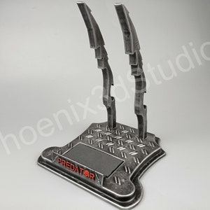 Puede incluir: Un soporte de metal con una base texturizada y tres cuchillas de metal. El soporte tiene la palabra "PREDATOR" impresa en rojo.