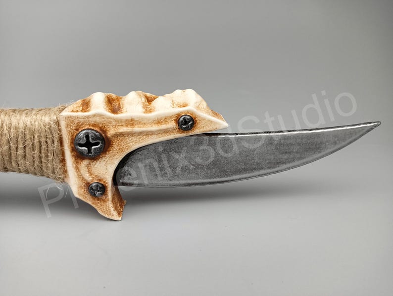 May include: A close-up of a knife with a bone-like handle and a curved blade. The handle is textured and has two screws. The blade is silver and has a sharp point.
