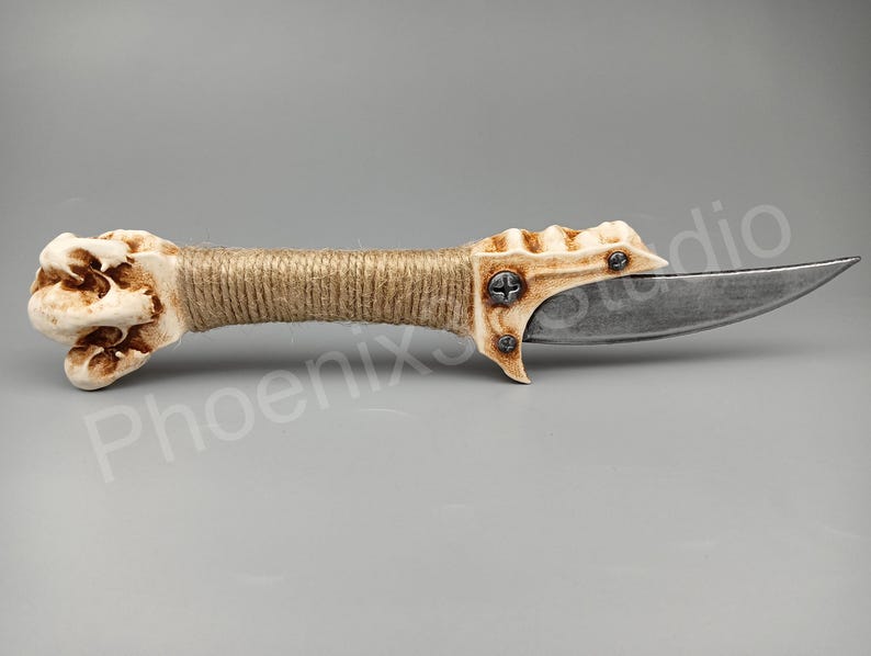 May include: A bone-handled knife with a brown twine wrap and a silver blade. The handle is sculpted to resemble a hand with a textured surface.