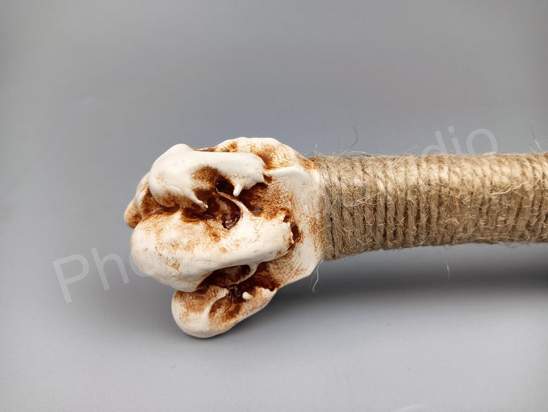 May include: A white ceramic sculpture with a rough, textured surface. The sculpture is shaped like a hand with brown rope wrapped around the wrist.