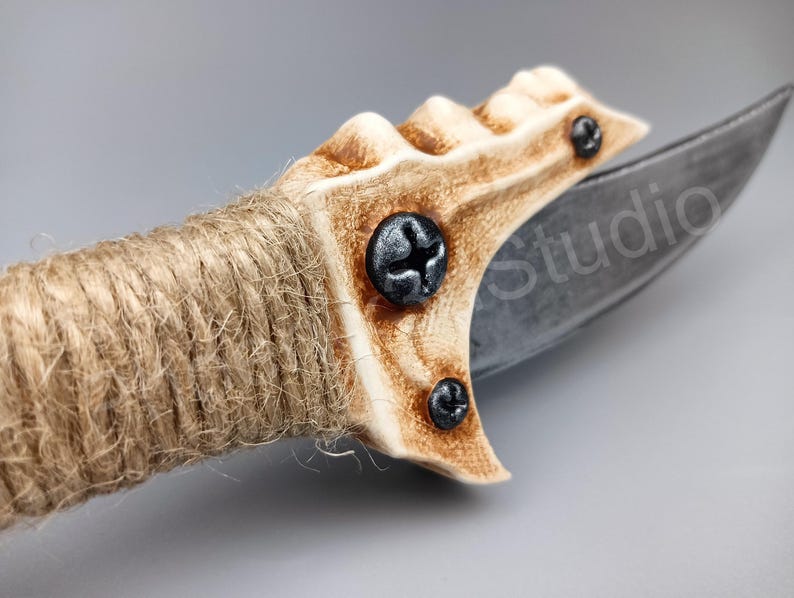 May include: A close-up of a knife with a brown and white handle wrapped in twine. The handle has a unique, textured design and is secured with screws. The blade is made of metal and has a sharp point.
