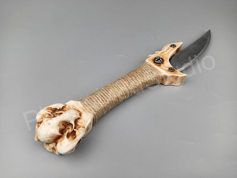 May include: A hand-crafted dagger with a bone handle, wrapped in twine, and a curved blade. The blade is made of metal and has a dark grey finish.