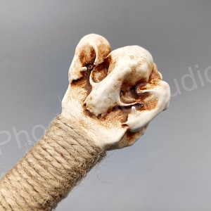 May include: A white ceramic skull with brown accents, wrapped in twine, is a decorative handle for a walking stick.