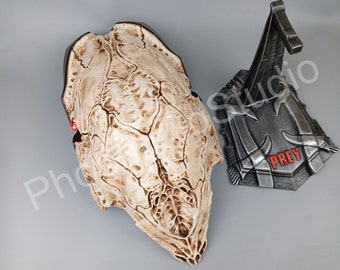 May include: A white Predator skull replica with red glowing eyes. The skull is displayed on a metal stand with the word "PREY" printed on it.