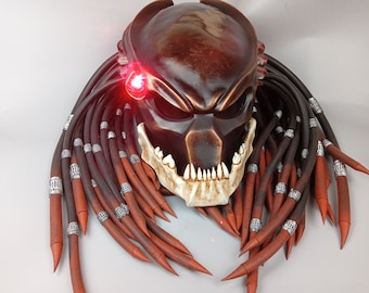 May include: A brown Predator helmet with red glowing eyes and dreadlocks. The dreadlocks are made of brown and red material with silver accents.