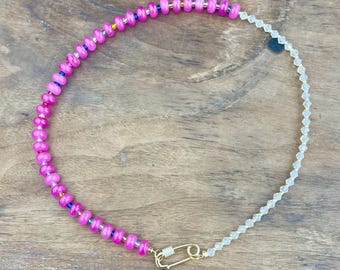 May include: A necklace featuring a combination of bright pink and clear beads. The pink section is made of round beads, while the clear section is made of smaller, faceted beads. A gold-colored clasp secures the necklace.