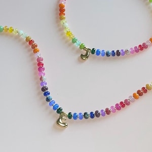 Peut inclure: Deux colliers de perles aux couleurs de l'arc-en-ciel avec des breloques initiales dorées. Les perles passent par un spectre de couleurs, du vert au rouge. Un collier porte l'initiale "E", l'autre l'initiale "J".