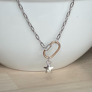 May include: Silver-toned chain necklace with a gold-colored clasp and a small, silver star pendant. The necklace has a simple, elegant design, perfect for everyday wear. The chain is made of small, oval links.
