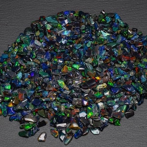 Puede incluir: Una colección de pequeños fragmentos de ópalo oscuros e irregulares que presentan destellos vibrantes de colores iridiscentes en verde, azul y rojo. Estas astillas de piedras preciosas pulidas tienen un acabado brillante.
