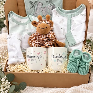 May include: A gift box containing a sage green bib with embroidered animals, a striped bodysuit, a white patterned sleeper, a plush giraffe toy, two ceramic mugs labelled Mummy's Mug and Daddy's Mug, and a pair of sage green knitted baby booties.
