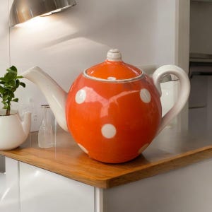 May include: A large orange teapot with white polka dots. The teapot has a white lid and a white handle.
