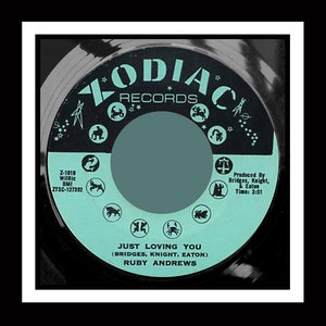 May include: A turquoise vinyl record with a black label. The label features the text "ZODIAC RECORDS" in a white circle with black stars and zodiac symbols. The record title is "JUST LOVING YOU (BRIDGES, KNIGHT, EATON) RUBY ANDREWS".