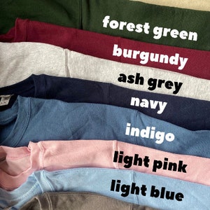 May include: A stack of ten sweatshirts in different colors, including sand, forest green, burgundy, ash grey, navy, indigo, light pink, light blue, and charcoal.
