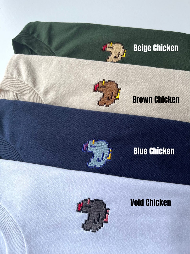 May include: Four t-shirts with different colored pixelated chicken designs. The shirts are stacked on top of each other. The designs are beige, brown, blue, and gray. The text on the shirts reads "Beige Chicken", "Brown Chicken", "Blue Chicken", and "Void Chicken".