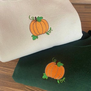 May include: Two sweatshirts with embroidered pumpkins. One sweatshirt is beige and the other is dark green.