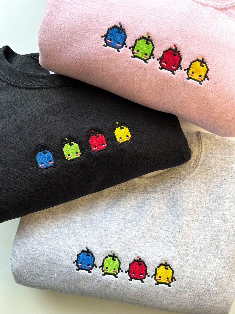 May include: Three sweatshirts in different colors, pink, black, and gray, with embroidered pixelated characters in blue, green, red, and yellow.