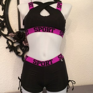 Peut inclure: Ensemble de sport noir composé d'un soutien-gorge et d'un short avec des bordures roses et le mot "SPORT" imprimé en noir sur les bordures.