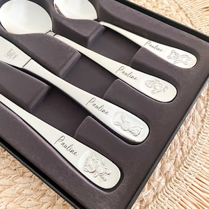 May include: A four-piece stainless steel cutlery set in a black presentation box. Each piece features the name Pauline engraved in script, along with a unique embossed animal character including a bear, a monkey, a rabbit, and a cat.