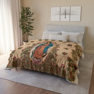 May include: A beige fleece blanket with a floral pattern featuring a depiction of the Virgin Mary in a blue and red robe. The blanket is on a bed with white pillows.