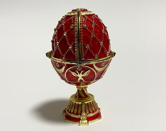 May include: A red decorative egg-shaped trinket box with gold accents. The egg features a diamond pattern with embedded crystals and opens to reveal a compartment. The base is gold with a detailed design.