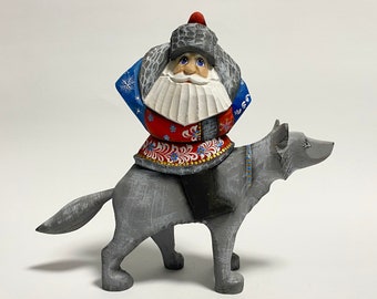 May include: A hand-carved wooden figurine of a bearded figure in a red and blue coat and hat, riding a gray wolf. The figure has a white beard and blue eyes. The wolf has a saddle and a blue collar.