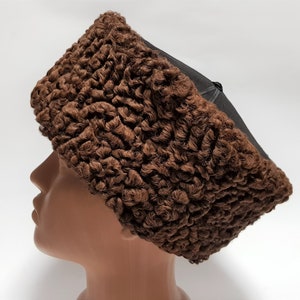 May include: A brown fur hat with a black felt top. The hat is made of curly fur and has a rounded shape.