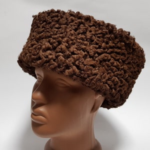May include: A brown fur hat with a curly texture. The hat is worn on a mannequin head.