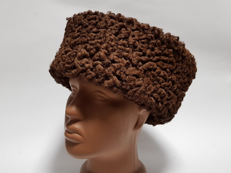 May include: A brown fur hat with a curly texture. The hat is worn on a mannequin head.