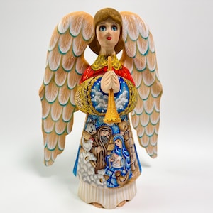 May include: A hand-painted angel figurine with large, detailed wings. The angel wears a red and gold garment and holds a golden trumpet. The angel's skirt depicts a nativity scene. A decorative item for the holidays.