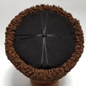May include: A brown fur hat with a black felt top and a black ribbon tied in a knot at the centre.