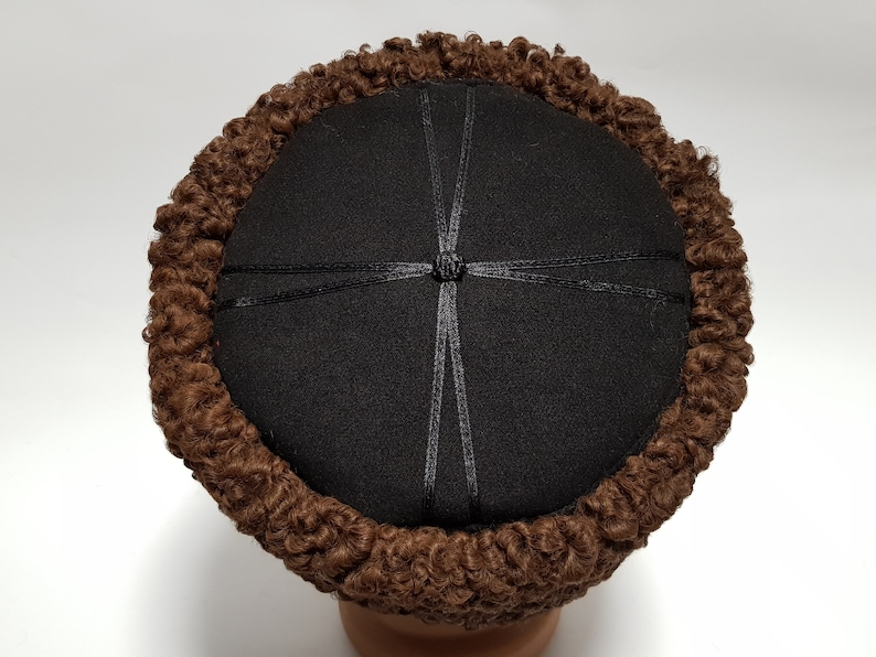 May include: A brown fur hat with a black felt top and a black ribbon tied in a knot at the centre.