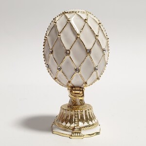 May include: A white porcelain egg with a gold lattice design and clear rhinestones. The egg is on a gold stand with a white base.