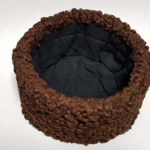 May include: A brown fur hat with a black quilted lining. The hat is made of a soft, fluffy material and has a round shape.