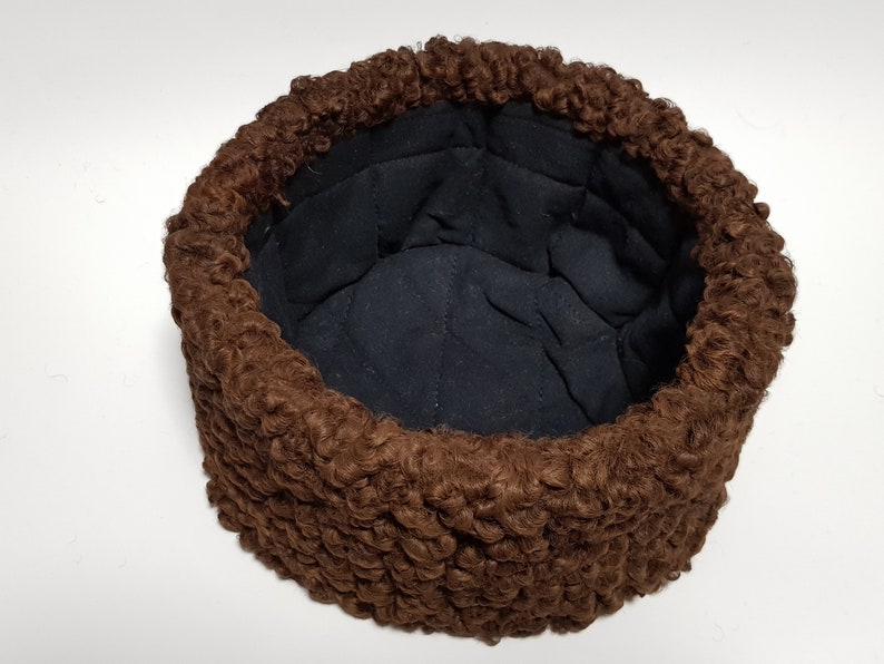 May include: A brown fur hat with a black quilted lining. The hat is made of a soft, fluffy material and has a round shape.