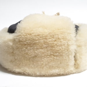 May include: A white sheepskin hat with a black leather brim. The hat is made of soft, fluffy sheepskin and has a warm, cozy feel.