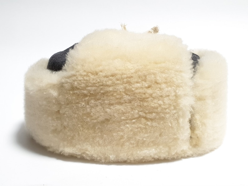 May include: A white sheepskin hat with a black leather brim. The hat is made of soft, fluffy sheepskin and has a warm, cozy feel.