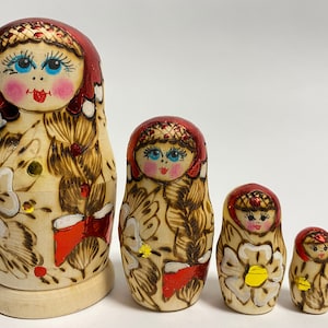 Puede incluir: Conjunto de cinco muñecas rusas tradicionales de anidación, o muñecas matrioska. Las muñecas están pintadas con diseños florales y presentan detalles en rojo, blanco y dorado. La muñeca más grande mide aproximadamente 25 cm de alto.