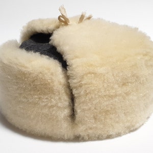 May include: A white faux fur hat with a black fabric lining. The hat has a fold-over flap and a string tie.