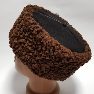 May include: A brown fur hat with a black felt top. The hat is round in shape and made of curly fur.