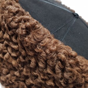 May include: A brown curly fur hat with a black felt top. The hat is made of sheepskin and has a traditional design.
