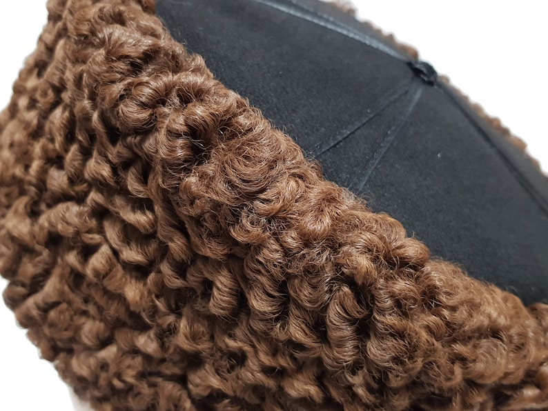 May include: A brown curly fur hat with a black felt top. The hat is made of sheepskin and has a traditional design.