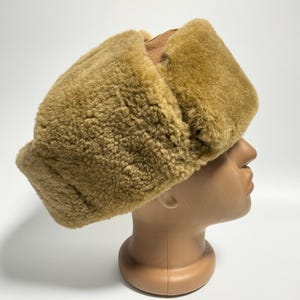May include: A brown faux fur hat with a fold-over flap. The hat is made of a soft, plush material and has a warm, cosy look.
