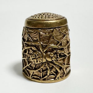 May include: A gold metal thimble featuring a spider and web design.