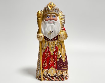 May include: A hand-painted wooden figurine of a jolly character with a long white beard, blue eyes, and a gold crown. The figure wears a red and gold patterned robe and holds a gold staff. A festive decorative item.