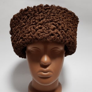 May include: A brown fur hat with a curly texture. The hat is worn on a mannequin head.