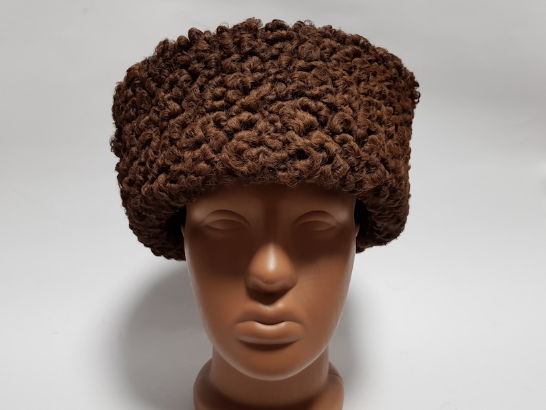May include: A brown fur hat with a curly texture. The hat is worn on a mannequin head.
