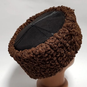 May include: A brown fur hat with a black leather top. The hat is round in shape and made from a soft, fluffy material.