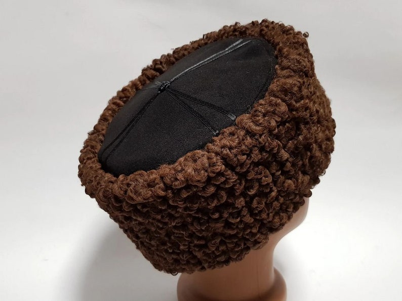 May include: A brown fur hat with a black leather top. The hat is round in shape and made from a soft, fluffy material.