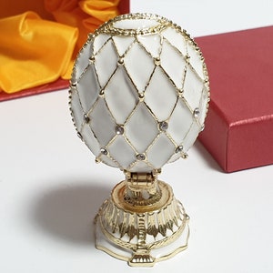 May include: A white porcelain egg with a gold lattice design and clear rhinestones. The egg is on a gold stand with a decorative base.